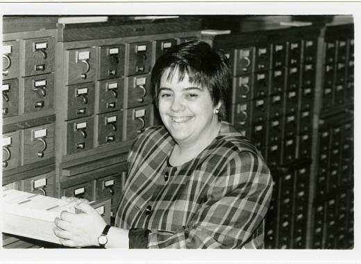woman with short hair and a plaid shirt opening drawer of a card catalog