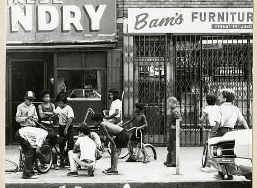 a group of twelve young children with their bikes gather in front of two storefronts in Coney Island