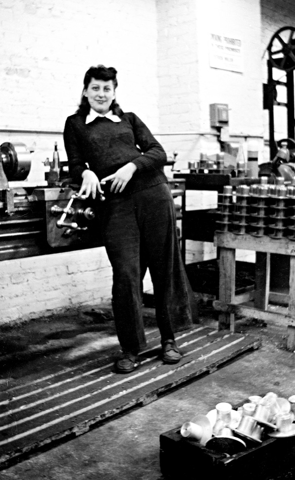 Photo of a woman with dark hair dressed in black, smiling in a factory setting.