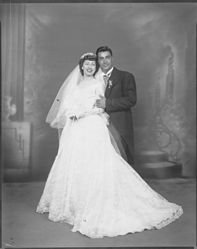 Wedding portrait of man and woman standing. Man is dressed in tuxedo woman is in white dress with bouquet.