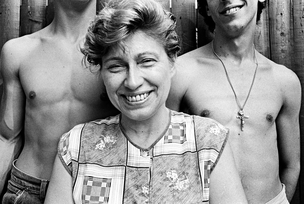 Older woman smiling with two young shirtless men, faces not visible behind her