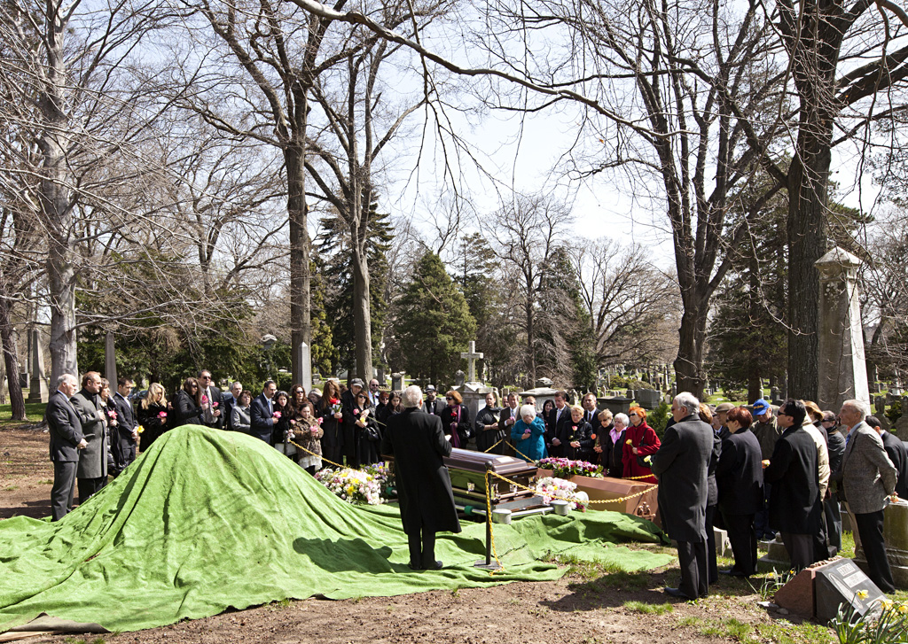 Photo of people gathered at a burial service outdoors in a cemetery