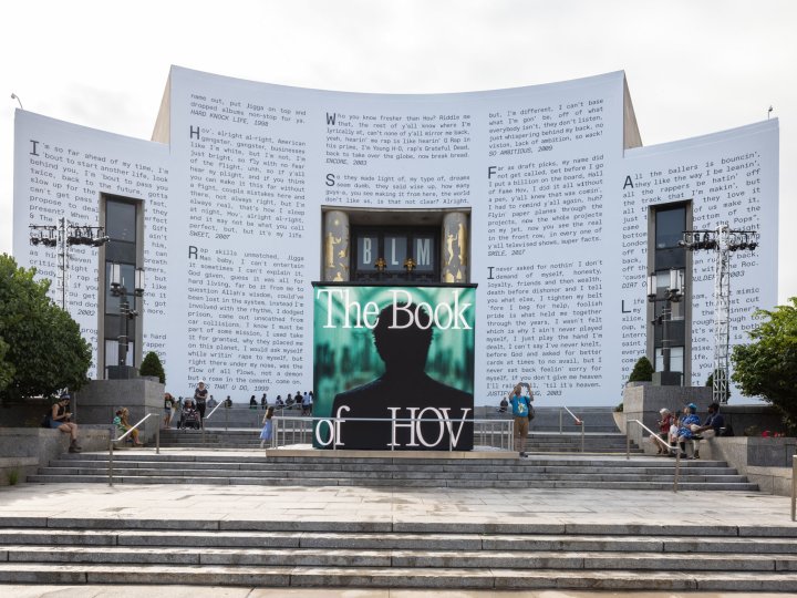 Brooklyn Public Library's Central Library facade wrapped in JAY-Z lyrics. In the foreground is a large cube playing music videos and displaying the words The Book of HOV