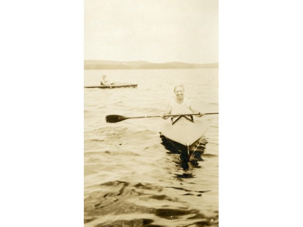 A sepia toned photo of two women in canoes on a river in Maine.